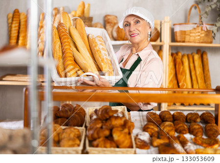 Senior female baker worker sells baguette, shows many products 133053609