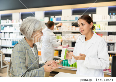 Girl apothecary hold package with cream and talks with senior woman client about nuances of care 133053624