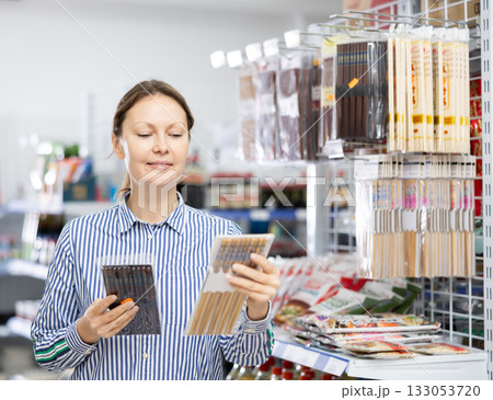 Smiling female shopper choosing bamboo chopsticks in Asian store 133053720