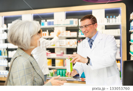 Man apothecary hold package with cream and talks with senior woman client about nuances of care 133053760