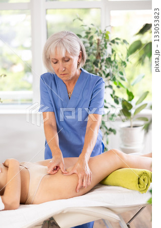 Elderly woman giving thigh massage to young woman Elderly woman giving thigh massage to young woman 133053823