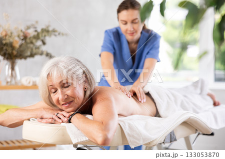Blurry unrecognizable woman performs shoulder massage to female client. 133053870
