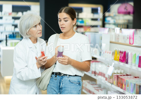 Girl buyer and an elderly woman pharmacist select intimate hygiene items together in pharmacy Girl buyer and an elderly woman pharmacist select intimate hygiene items together in pharmacy 133053872