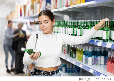Girl customer is thinking about buying spicy and unusual Korean soy wine chum churum. 133053894
