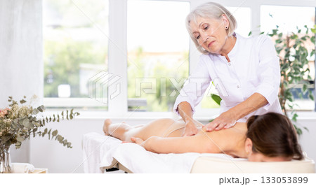 Skilled aged masseuse doing back pain relief massage to young woman Skilled aged masseuse doing back pain relief massage to young woman 133053899