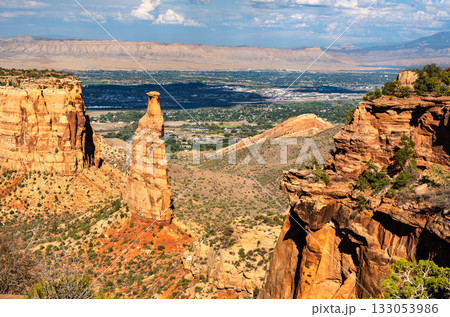 View of the iconic Independence Monument spire in Colorado National Monument. The Grand Valley and Book Cliffs are visible in the background 133053986