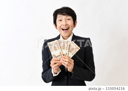 札束を持ち驚くスーツ姿の笑顔のミドル女性 札束を持ち驚くスーツ姿の笑顔のミドル女性 133054216