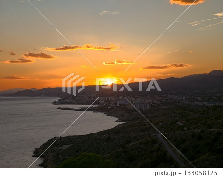 colorful dusk reflecting on water, bright horizon illuminates rugged shoreline with peaceful sea 133058125