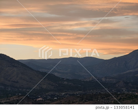 serene sunset bathed in pastel hues illuminates rolling hills and towering distant mountain peaks serene sunset bathed in pastel hues illuminates rolling hills and towering distant mountain peaks 133058141