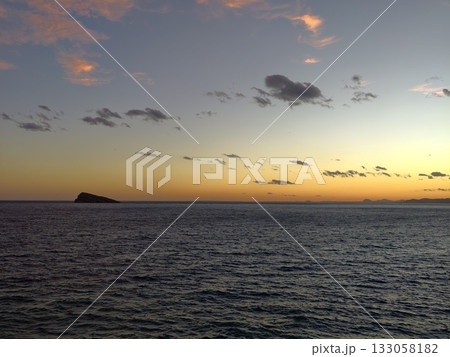 jagged peak against calm ocean horizon, clifflike formation silhouetted by gentle evening glow 133058182