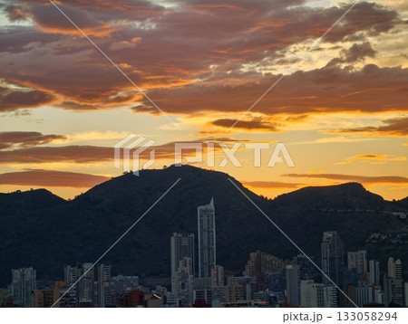 vivid sunset scene, evening sky paints vibrant picture with towering mountains and urban silhouettes 133058294