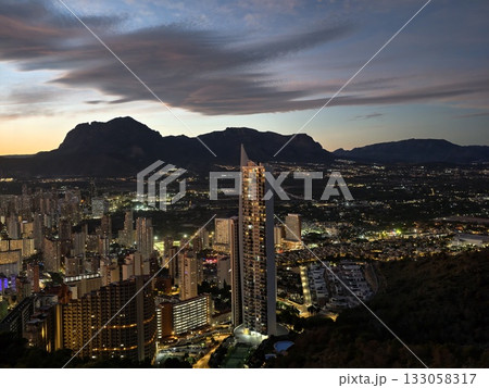 nighttime urban scene with mountains, sunset over city with mountain silhouette and glowing windows 133058317