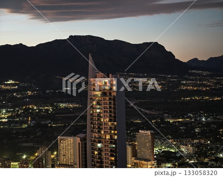 contemporary skyscraper visuals, sleek glass building with mountain background and illuminated 133058320