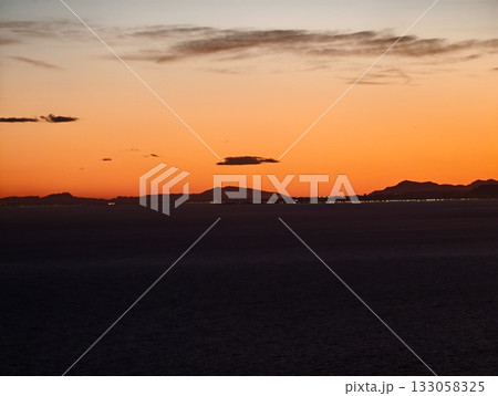 calm evening sheen highlighting rugged mountains and glowing shoreline with distant illumination 133058325