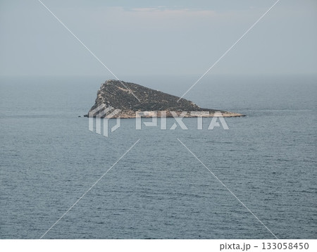 single coneshaped islet amidst peaceful waters, serene solitary landform beneath soft sky tones 133058450