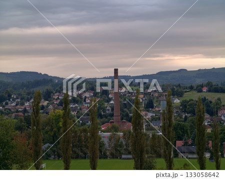 silhouetted trees contrast evening moody sky, hilltop observer watches town and smokestack at dusk silhouetted trees contrast evening moody sky, hilltop observer watches town and smokestack at dusk 133058642