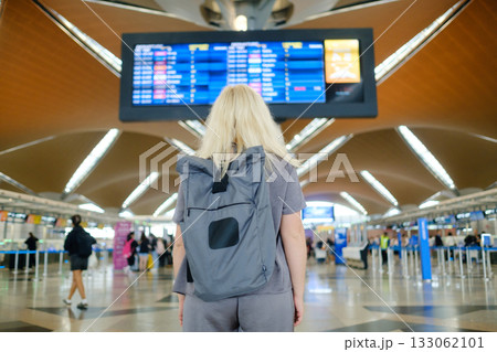 Person with backpack looking at flight information display in busy airport terminal during daytime 133062101