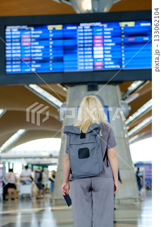Traveler waiting at the airport terminal looking at the flight information board displaying departure and arrival times in a busy travel environment Traveler waiting at the airport terminal looking at the flight information board displaying departure and arrival times in a busy travel environment 133062104