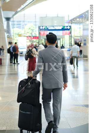 Business traveler in smart suit walking through bustling airport terminal with suitcase in tow during the day Business traveler in smart suit walking through bustling airport terminal with suitcase in tow during the day 133062108