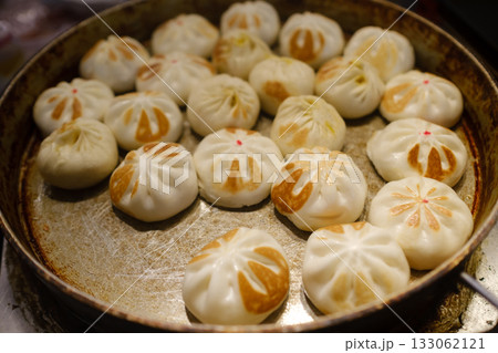 Delicious dumplings being cooked in a round pan at a bustling market during the afternoon, showcasing a mix of colors and textures that invite hungry food lovers Delicious dumplings being cooked in a round pan at a bustling market during the afternoon, showcasing a mix of colors and textures that invite hungry food lovers 133062121