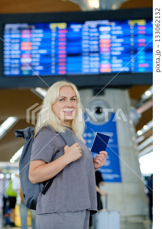 Woman at airport checking flight information while holding her passport and standing near departure board 133062132