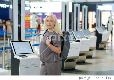 Woman with backpack interacting with check-in kiosk in modern airport terminal during busy travel season 133062135