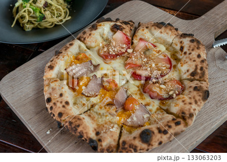 カッティングボードにのった焼き立てピザがパスタとともに店内のテーブルに並ぶ カッティングボードにのった焼き立てピザがパスタとともに店内のテーブルに並ぶ 133063203