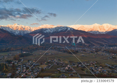 紅葉に染まる八方尾根スキー場と冠雪した白馬連峰のモルゲンロート　長野県白馬村（ドローンによる空撮） 133064579