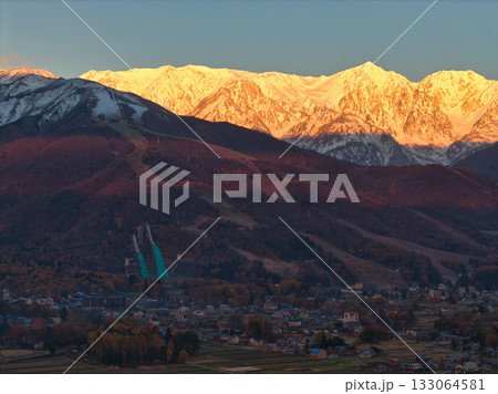 紅葉に染まる八方尾根スキー場と冠雪した白馬連峰のモルゲンロート　長野県白馬村（ドローンによる空撮） 133064581