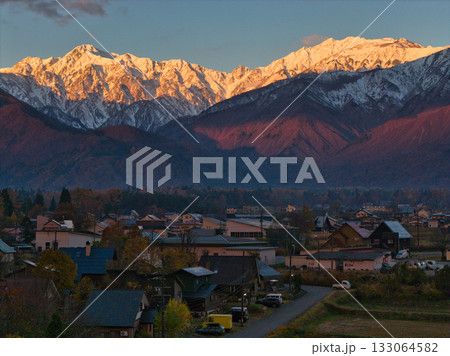 紅葉に染まる里山と冠雪した五竜岳・唐松岳のモルゲンロート　長野県白馬村（ドローンによる空撮） 133064582