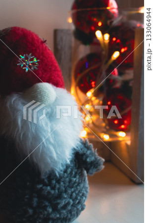 Scandinavian gnome with Christmas lights, vertical. Swedish Santa Claus and warm bulb garland, close up. Christmas decoration and toys. New Year mood. Festive illumination and Christmas gnome 133064944