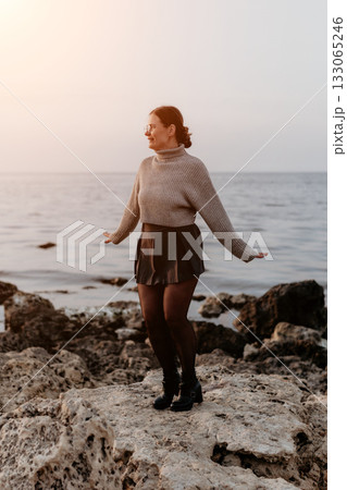 Woman Beach Sunset Joyful Pose: Coastal Rocks, Evening Happiness, Autumnal Fashion. Woman Beach Sunset Joyful Pose: Coastal Rocks, Evening Happiness, Autumnal Fashion. 133065246