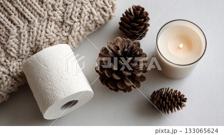 Minimal winter flat lay with toilet paper candle and pinecones on soft fabric 133065624