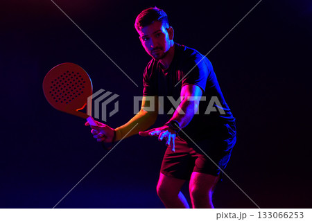 Man plays paddle tennis in vibrant lighting with focus on technique and movement 133066253