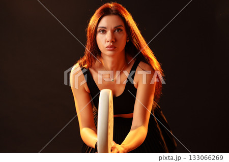 Woman poses with fitness hoop in a dark studio setting during a dynamic photoshoot session 133066269
