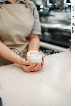 Warm cup of coffee held by a barista in a cozy cafe setting during daytime 133066275