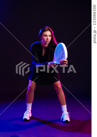 Woman preparing to play padel in a colorful studio setting with dramatic lighting 133066300