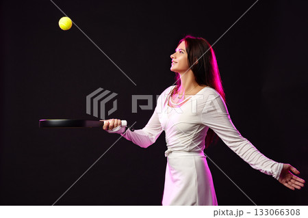 Woman practices tennis indoors while smiling at the ball in a dynamic pose Woman practices tennis indoors while smiling at the ball in a dynamic pose 133066308