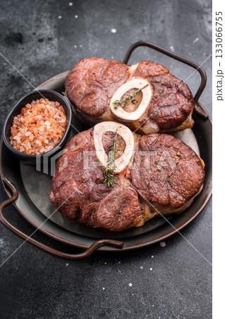 Deliciously braised ossobuco, featuring tender osso buco veal shank and rich marrow, perfect for a gourmet Italian feast. black background. top view Deliciously braised ossobuco, featuring tender osso buco veal shank and rich marrow, perfect for a gourmet Italian feast. black background. top view 133066755
