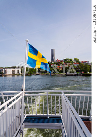 Swedish flag with colony of small wooden historic houses on the Slottsberget mountain with the tallest Scandinavian building Karlatornet skycraper in Lindholmen in background, Gothenburg, Sweden Swedish flag with colony of small wooden historic houses on the Slottsberget mountain with the tallest Scandinavian building Karlatornet skycraper in Lindholmen in background, Gothenburg, Sweden 133067116