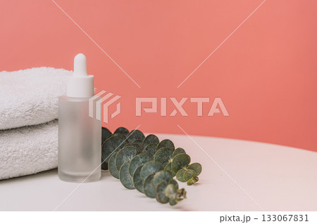 Glass dropper bottle with eucalyptus and towels on pink background Glass dropper bottle with eucalyptus and towels on pink background 133067831
