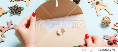 Top view of woman holding an envelope on blue background made of holiday decorations. Christmas time concept Top view of woman holding an envelope on blue background made of holiday decorations. Christmas time concept 133068379