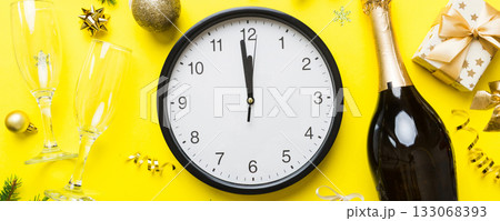 New year celebration concept with a bottle of champagne and two glasses toasting. Christmas gift box, alarm clock and fir tree branch on colored table. Top view Copy space New year celebration concept with a bottle of champagne and two glasses toasting. Christmas gift box, alarm clock and fir tree branch on colored table. Top view Copy space 133068393
