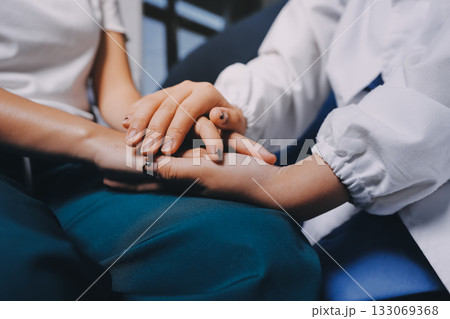 Doctor giving hope. Close up shot of young female physician leaning forward to smiling elderly lady patient holding her hand in palms. Woman caretaker in white coat supporting encouraging old person Doctor giving hope. Close up shot of young female physician leaning forward to smiling elderly lady patient holding her hand in palms. Woman caretaker in white coat supporting encouraging old person 133069368