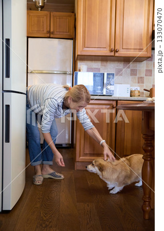 Senior Woman Playing With Corgi Dog in Kitchen Senior Woman Playing With Corgi Dog in Kitchen 133070470