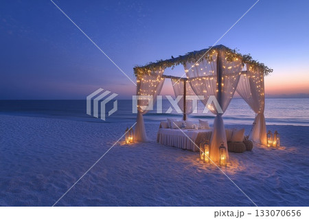 Romantic beach dining experience under twinkling lights at sunset with softly lapping waves in the background 133070656