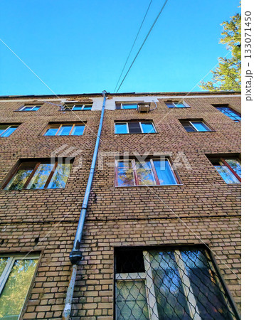 Upward view of an old brick apartment facade with a long metal downpipe, patch repairs near the roof and an external AC unit. Useful for content about brick repointing, drainage replacement, window Upward view of an old brick apartment facade with a long metal downpipe, patch repairs near the roof and an external AC unit. Useful for content about brick repointing, drainage replacement, window 133071450