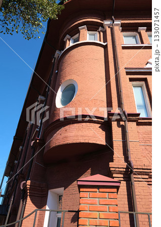 Close-up view of a red brick building corner with a rounded bay window and circular glazing element, showcasing historic masonry craftsmanship and classic drainage design. Suitable for content about 133071457