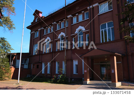 Street view of a historic red brick institutional building with arched windows, white keystones and a small entrance canopy in even daylight. Relevant for ads about masonry restoration, facade 133071458