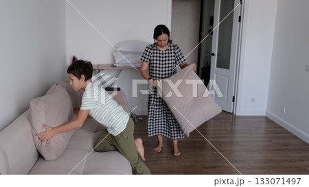 A woman and her son clean up the room, arranging soft cushions with calm focus in minimalist space. Such collaboration fosters respect, care, and good habits important for emotional growth. A woman and her son clean up the room, arranging soft cushions with calm focus in minimalist space. Such collaboration fosters respect, care, and good habits important for emotional growth. 133071497
